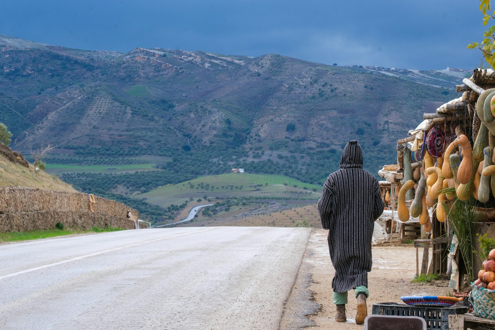 Man walks along a road with produce stand