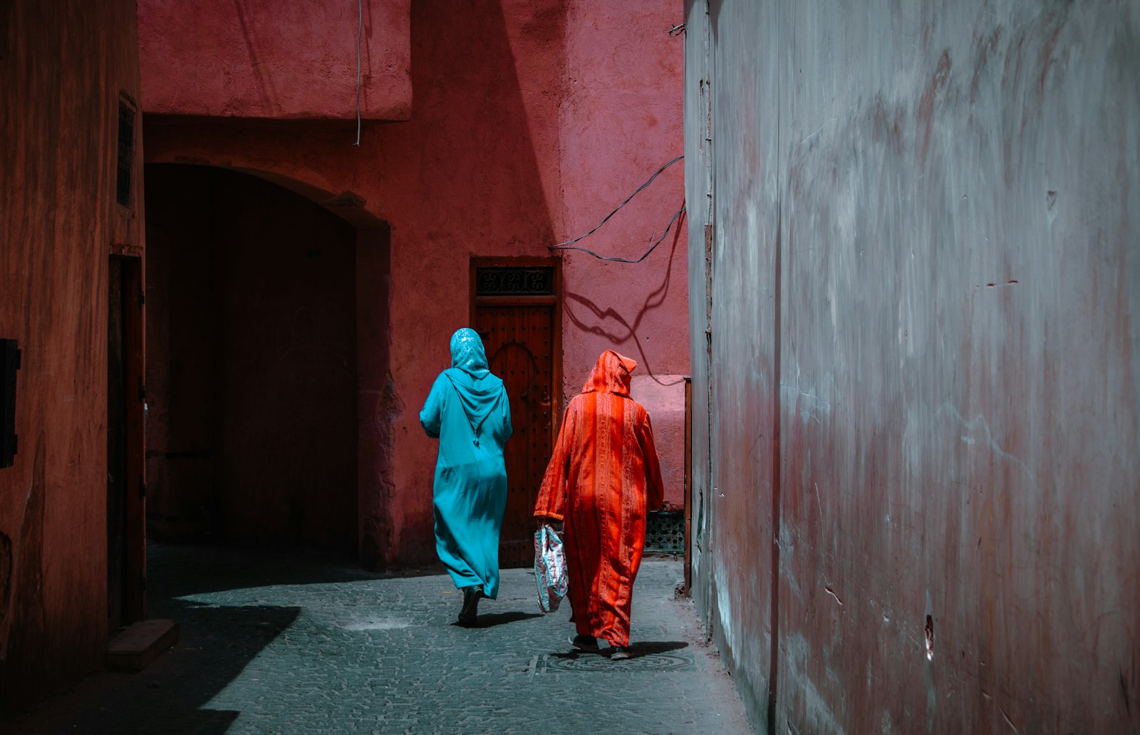 Two figures walk down a pink-walled alley.