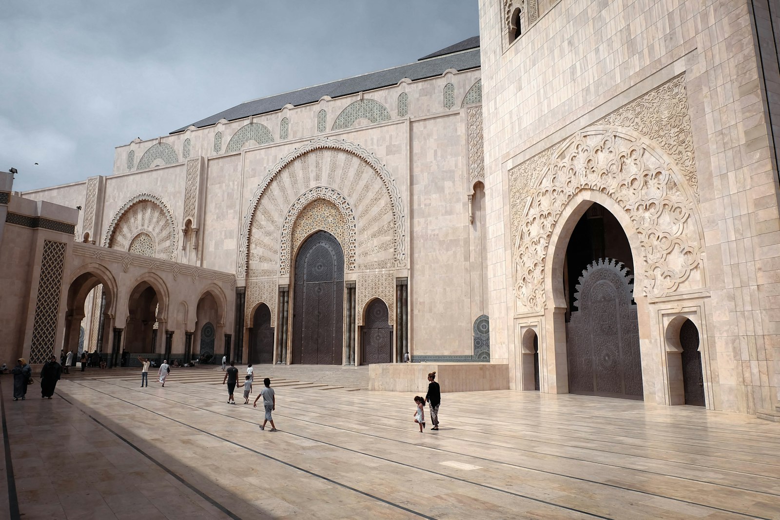 Grand mosque courtyard with people walking on pavement.