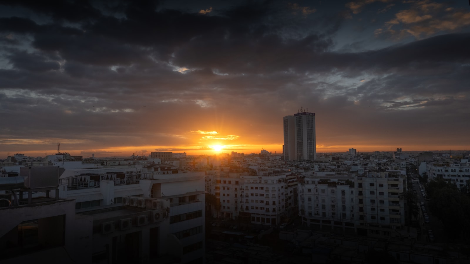 Sunset over a city skyline with cloudy skies.