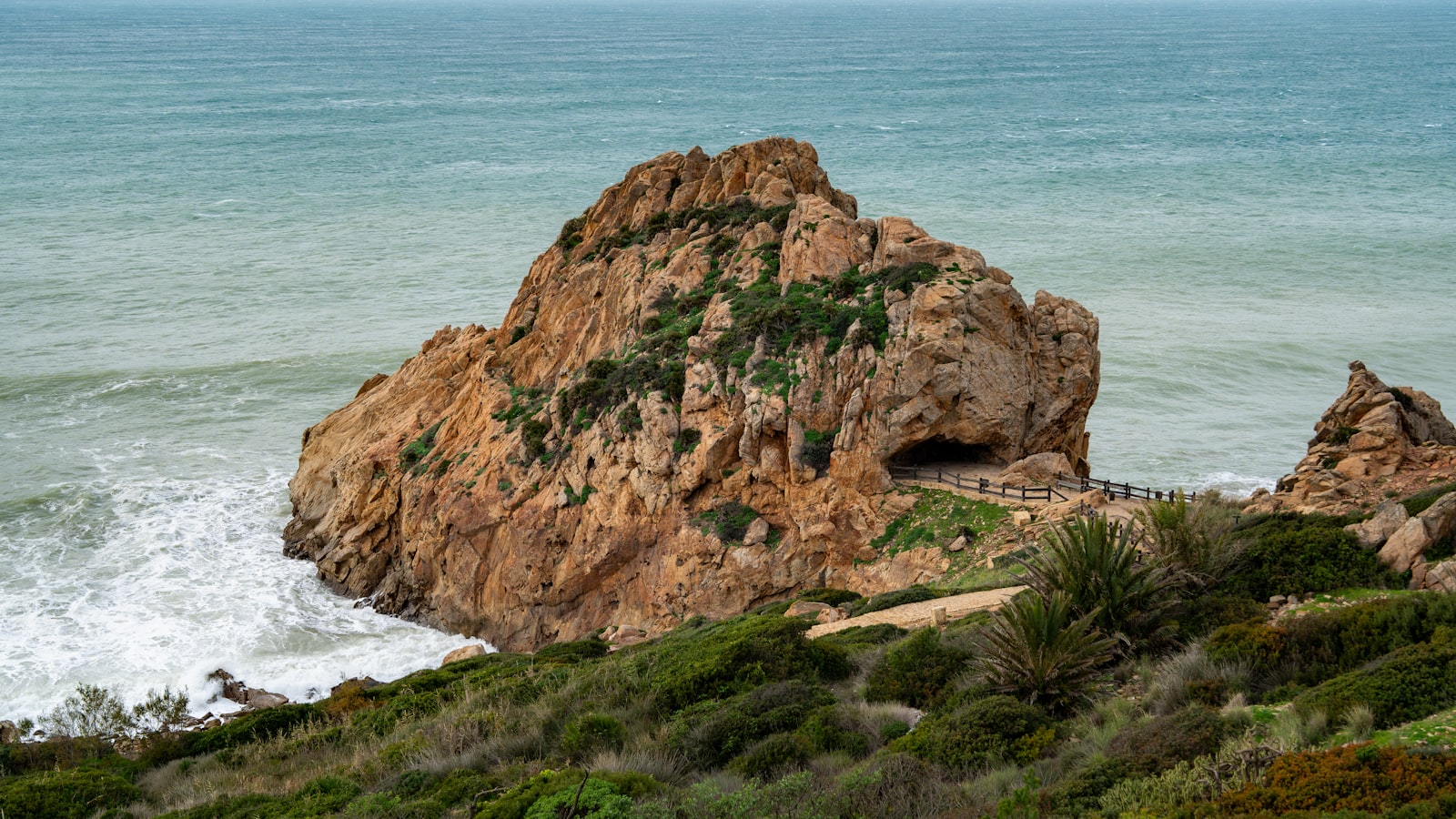 Large rock formation on a coastline with crashing waves.
