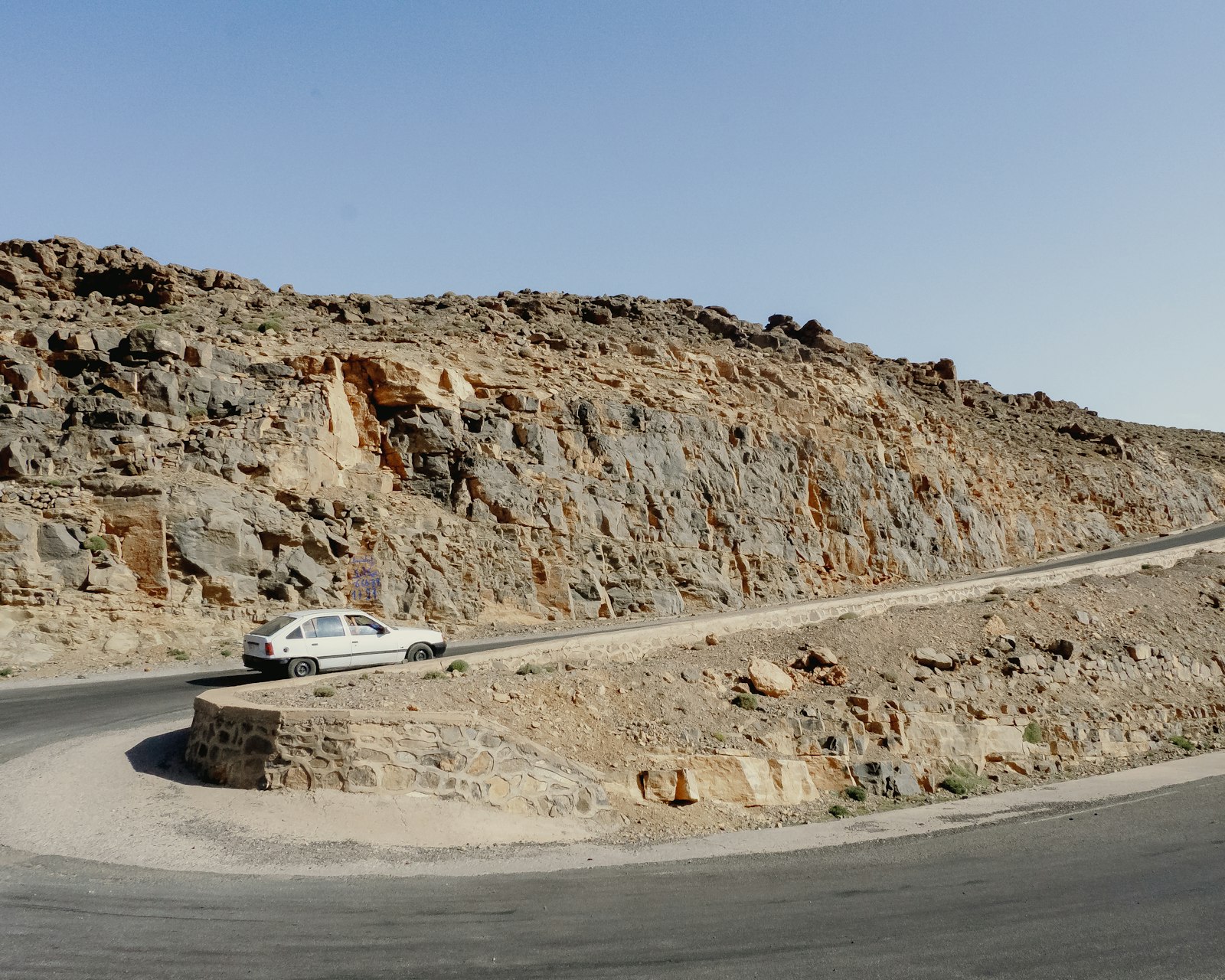 White car driving on a winding road through rocky terrain