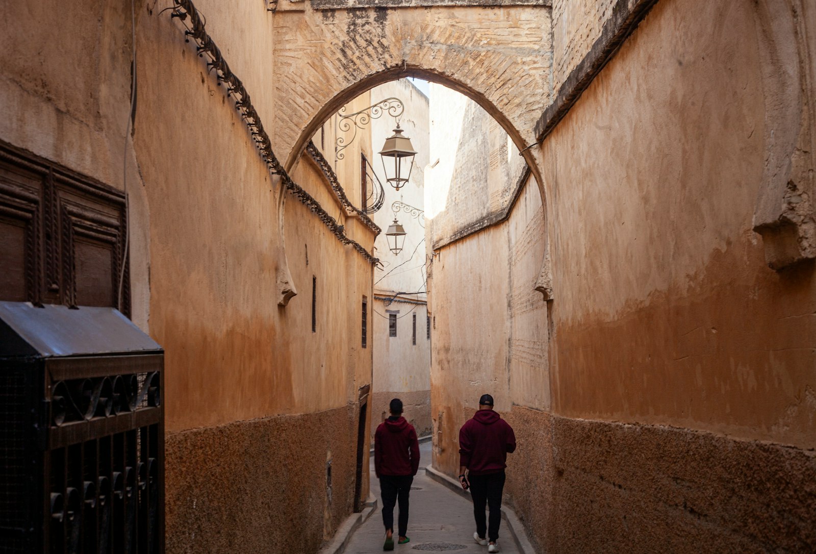 Two people walk down a narrow, arched alleyway