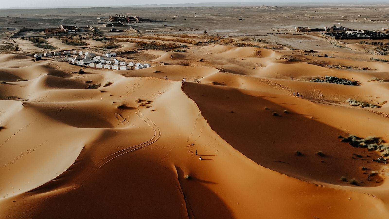 Desert landscape with sand dunes and tents.